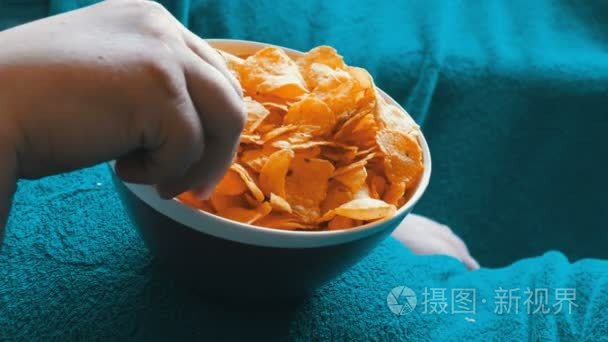 夫妇躺在一张蓝色毯子下的沙发上, 从一个男人肚子大的盘子里吃薯片