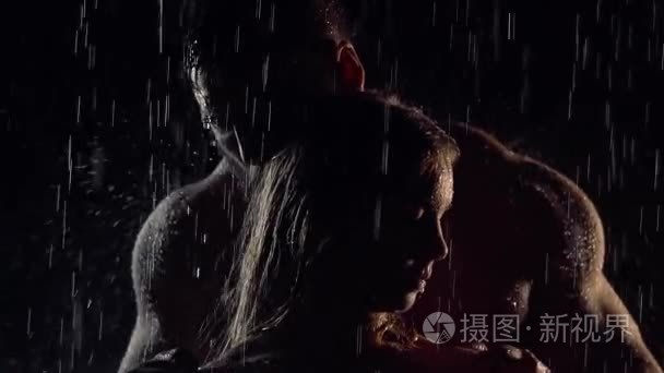 情侣们站在雨中  在黑暗中  粗壮的男人拥抱她的女人的肩膀