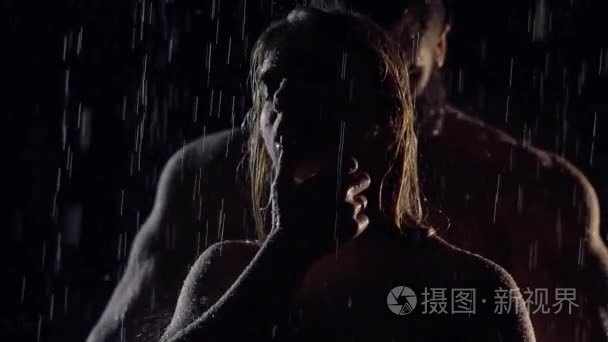 虚弱的女人和肌肉的男人在她背后的剪影,都站在雨中的夜晚