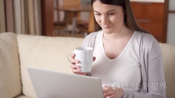 微笑的专业妇女在家里的笔记本电脑上工作喝咖啡。首页-办公理念