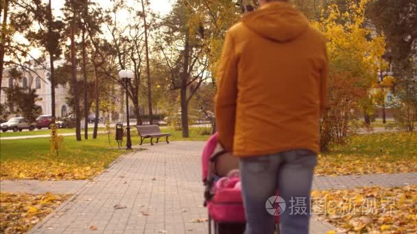 爸爸在秋季公园陪婴儿车散步。慢动作