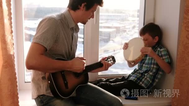演奏乐器。爸爸正在弹吉他  儿子在窗台上玩着铃鼓。