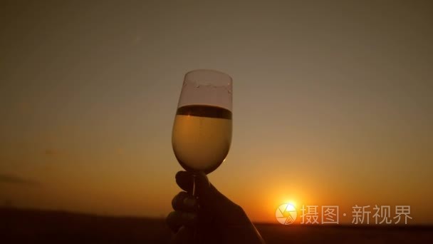 玻璃在手与美丽的日落背景的波光粼粼的酒