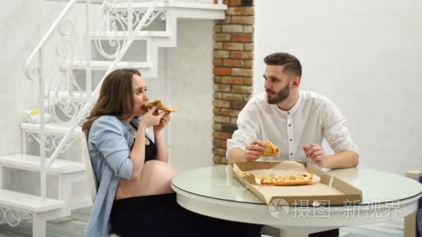 男子和孕妇在自家厨房吃比萨饼。欢笑乐趣