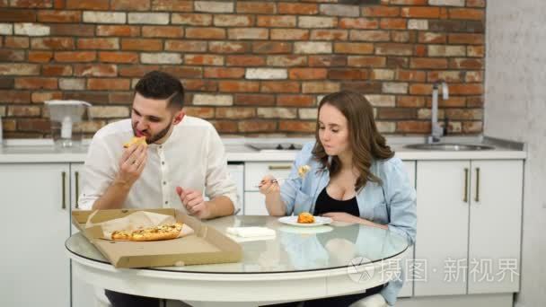 男子和孕妇在自家厨房吃比萨饼。糟糕的饮食。油腻的食物。肥胖