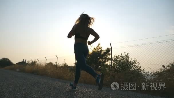 跟随对运动的女孩慢跑在乡间路在日出。晨跑户外的年轻女子。健康积极的生活方式。慢动作