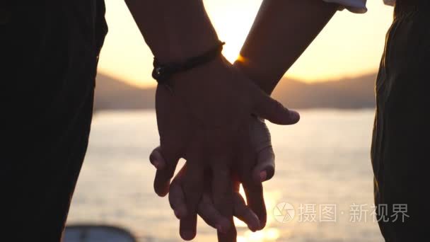 在日落时在海边的背景下男女手拉手的剪影年轻夫妇在