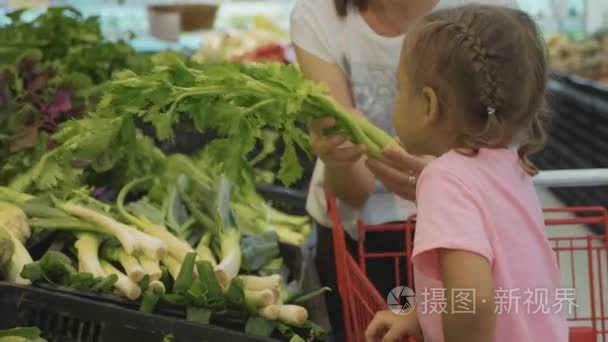 小女儿在杂货店里选择绿色蔬菜的年轻母亲