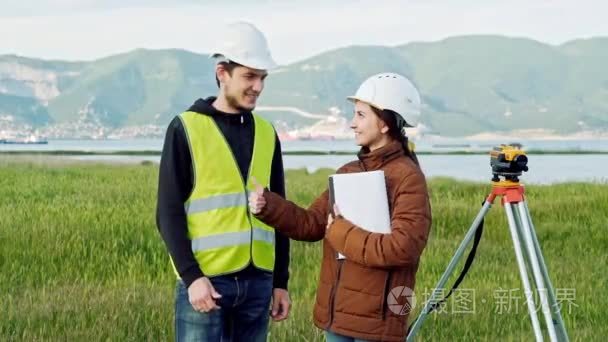 男女测量员在工作服和头盔上微笑着表示竖起大拇指, 这意味着良好的工作。景观设计的概念, 大地测量学