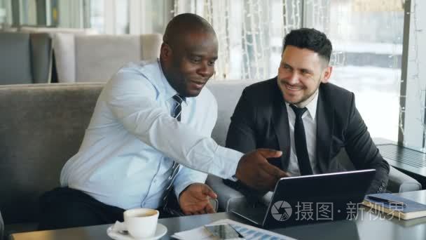 开朗的非洲裔美国商人在正式的衣服讨论商业项目与他的高加索同事在他的笔记本电脑在咖啡馆