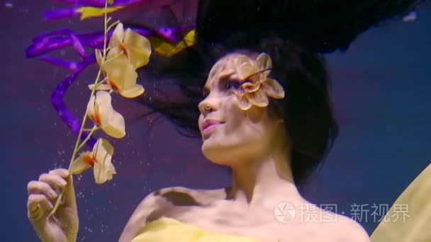 浪漫的微笑的女孩是水下  举行黄色兰花分支  影像嗅到的花朵