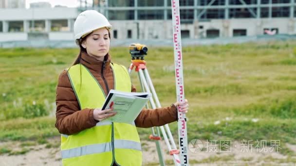 一名年轻女子的工作服和头盔的测量师调整设备  并在建筑工地上产生计算。景观设计的概念  大地测量学
