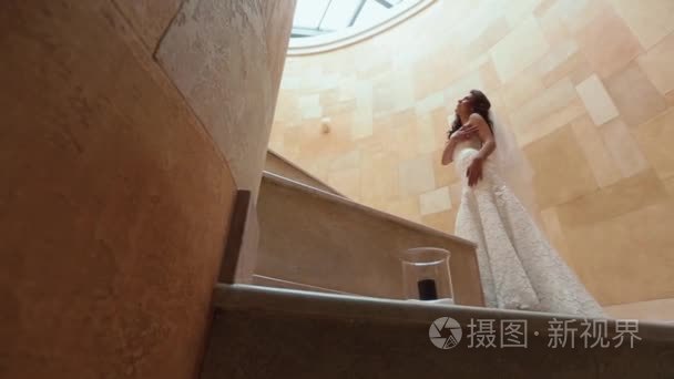 美丽的年轻新娘  黑色长卷发和时髦的婚纱礼服是摆在黄色的楼梯上。地板上蜡烛的景色