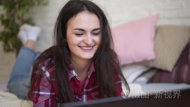 女人坐在床上  打开笔记本电脑。穿格子衬衫的黑发女孩