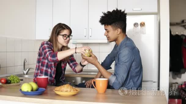 可爱的情侣一起吃苹果, 坐在他们的宽敞和明亮的舒适的厨房