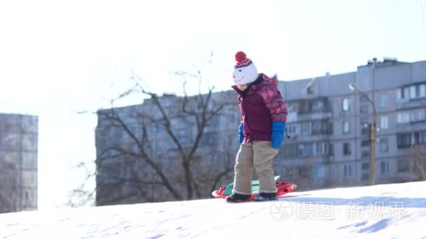 孩子在冬天散步。一个女孩骑在一个塑料盘子上的雪滑梯上