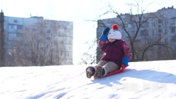 孩子在冬天散步。一个女孩骑在一个塑料盘子上的雪滑梯上