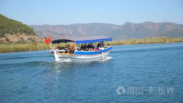 在阳光明媚的日子里  沿着海湾与游客一起漂浮的小船的侧面景色。在早上乘坐一条河的乘客船。美丽的山风景在背景。假期或假期的概念。特