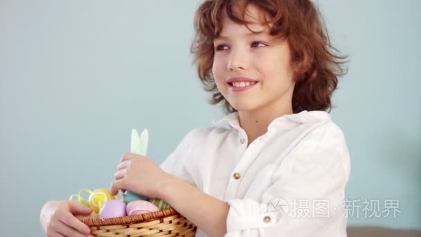快乐的小学生带着一篮子复活节彩蛋。卷曲头发的男孩笑乐趣