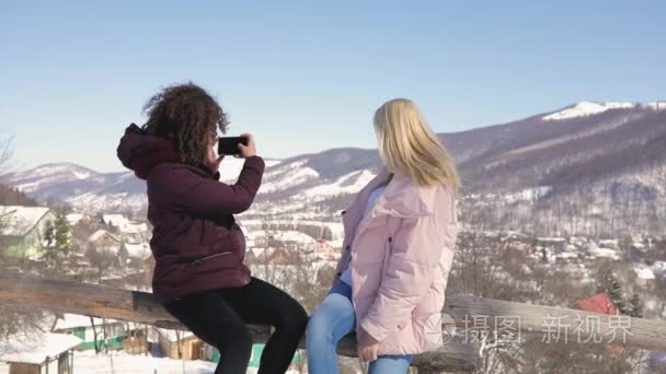 两个女孩的朋友在雪山背景上互相拍照