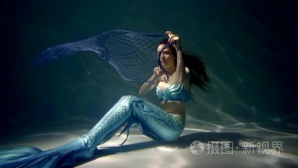 害怕的年轻美人鱼坐在海底, 找到一个渔网, 纠缠在其中, 向上移动短