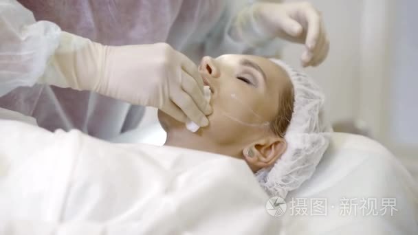 皮肤科医生用消毒的化合物擦拭病人的脸部以便做整容手术