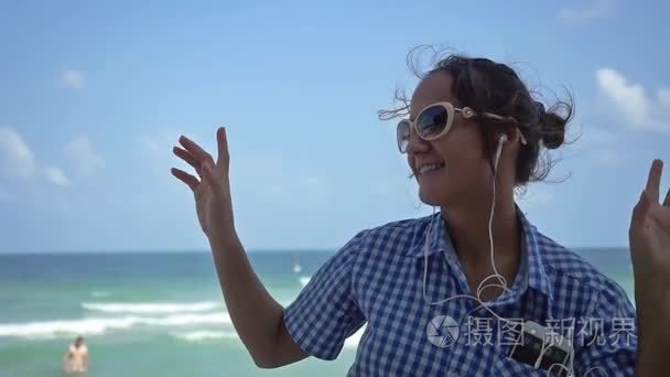 年轻漂亮的女人在太阳镜跳舞, 而在海边的海滩上听音乐的手机。慢动作。1920x1080