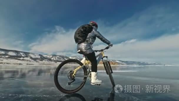 女人在冰上骑自行车。这个女孩穿着一件银色羽绒服  骑自行车背包和头盔。冰冻的贝加尔湖的冰。自行车上的轮胎布满了特殊的尖峰。