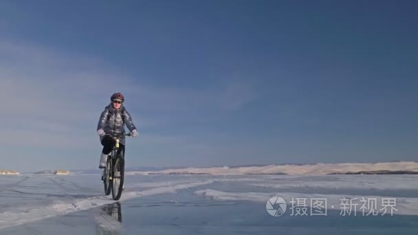 女人在冰上骑自行车。这个女孩穿着一件银色羽绒服  骑自行车背包和头盔。冰冻的贝加尔湖的冰。自行车上的轮胎布满了特殊的尖峰。