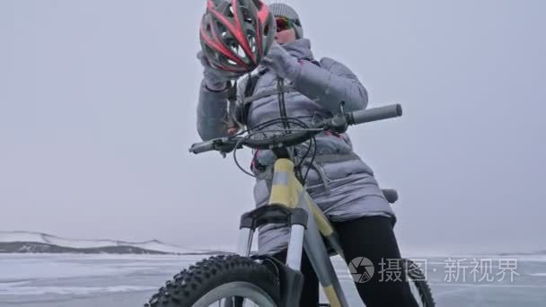 女人穿着运动器材。这个女孩穿着一件银色羽绒服  骑自行车背包和头盔。冰冻的贝加尔湖的冰。自行车上的轮胎布满了特殊的尖峰。