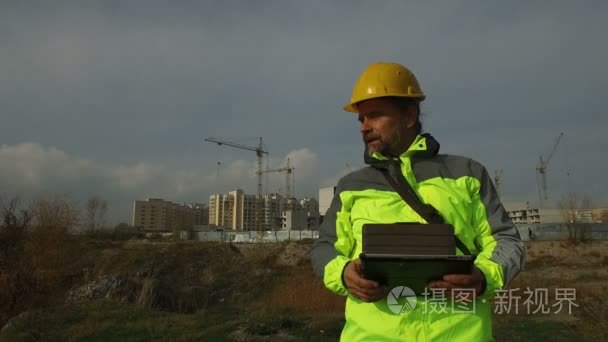 在建筑背景下使用平板头盔的成熟男职工工头