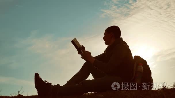 男学生在公园里看书, 背着背包日落。人读书剪影在天空生活方式日落自然温暖的口气