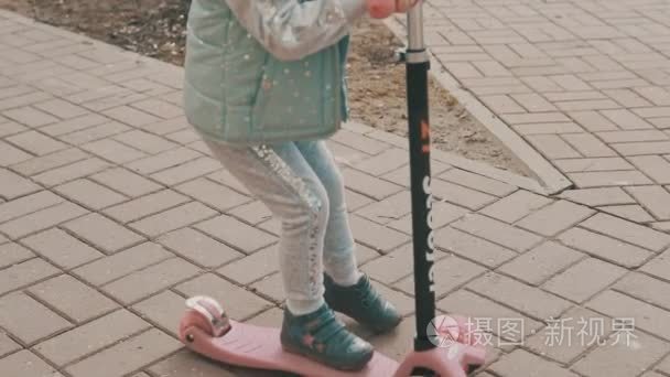 小女孩乘坐粉红色的滑板车在人行道上与 copyspace 在 slomo