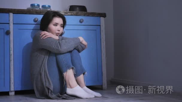 悲伤孤独的年轻亚洲女孩坐在地板上的厨房, 抱着她的膝盖与, 概念 50