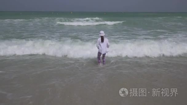 十几岁的女孩穿着衣服欢快地跳在波斯湾的海浪在迪拜的海滩上的股票录像视频