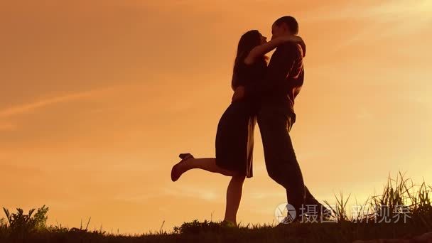 日落时分一对情侣的剪影。男人和女人的剪影在日落慢动作。相爱的情侣在日出时接吻。男人和女孩拥抱剪影生活方式家庭概念
