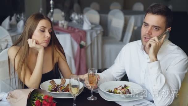 忙碌的年轻人正在用手机说话, 而他的女朋友却觉得坐在餐馆的餐桌上很无聊。现代技术关系与无聊概念视频
