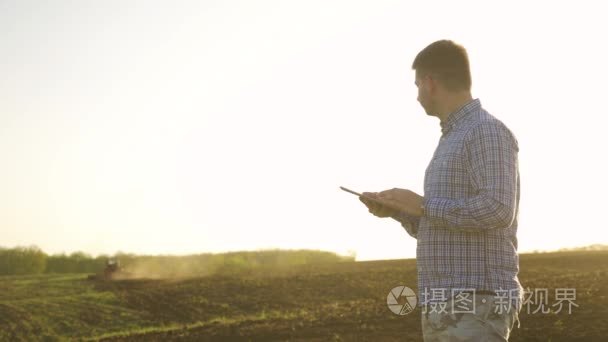 一个美丽的年轻人的画像农民工在田里干活, 用拖拉机在地里干活, 快乐, 在衬衣上沾污, 拖拉机的生活方式犁土地里。概念生态学