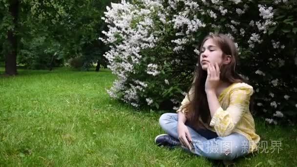 可爱的十几岁的女孩检查电话和等待的电话  坐在公园。视频素材高清拍摄静态相机