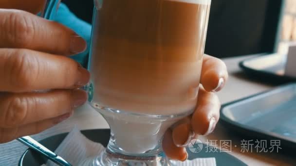 玻璃烧杯与咖啡  分级从深褐色到乳白色。咖啡里有一把大泡沫的漂亮拿铁咖啡。一个女人用热拿铁来碰玻璃