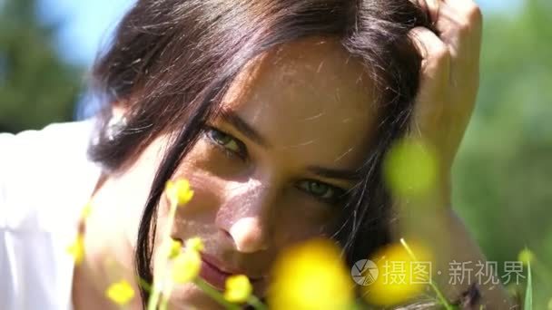 一个美丽的黑发妇女的肖像  户外  草坪上的绿草和黄色的花朵。她微笑着  用她的手在她的头发  可以看到一个美丽的耳环在她的耳朵