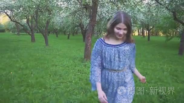 年轻女子在苹果园里奔跑, 春天的花朵是白色的。一个美丽的女孩在晚上的水果花园的肖像