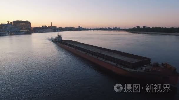 驳船在日落空中拍摄的城市港口附近的河流航行