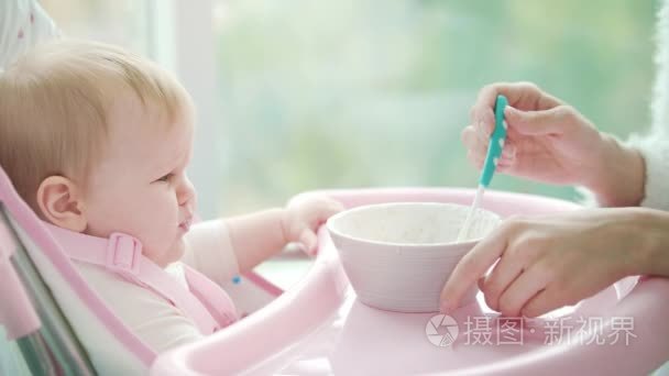 伤心的宝宝不想吃粥。小婴孩在椅子不吃膳食