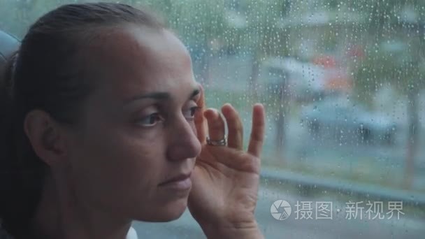 年轻悲伤的女人的肖像看着窗外的湿窗  而乘公共汽车旅行