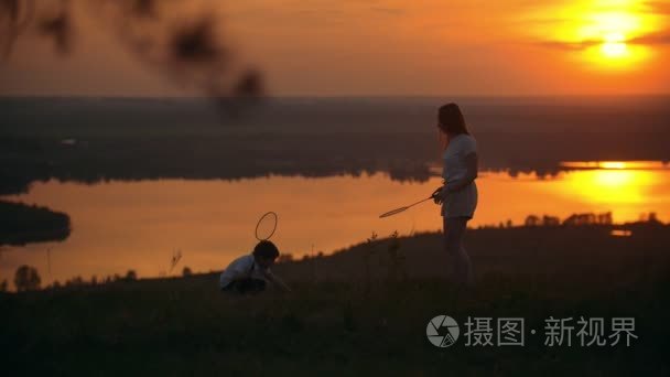 小男孩与他的大姐姐在山上打羽毛球在日落