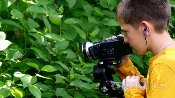 年轻男孩用摄像机拍摄关于自然的绿色公园背景的电影