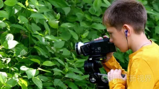 年轻男孩用摄像机拍摄关于自然的绿色公园背景的电影
