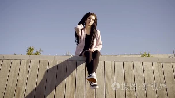 年轻的女孩坐在屋顶上倒挂在黑色紧身裤和运动鞋.