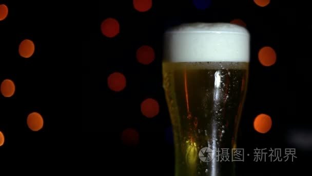 酒吧里有一杯带有彩色灯的黑色背景的冰镇啤酒。啤酒在玻璃中起泡
